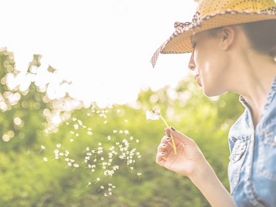 Frau mit behandeltem Heuschnupfen (oder Pollenallergie) hält eine Pusteblume in der Hand