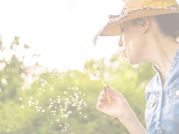 Frau kennt den aktuellen Pollenflug, auf den sie nicht reagiert und hält eine Pusteblume in der Hand