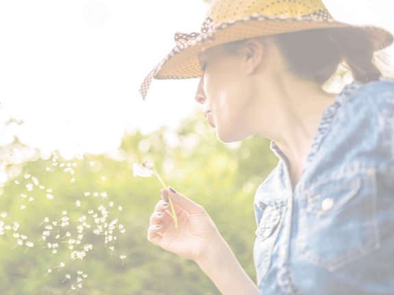 Frau kennt den aktuellen Pollenflug, auf den sie nicht reagiert und hält eine Pusteblume in der Hand