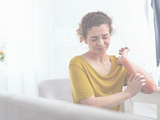 Eine Frau hat schmerzende Neurodermitis am Arm, was auch Folge einer Hausstauballergie sein kann.