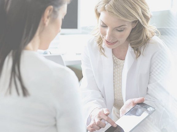 Ein Ärztin zeigt einer Patientin auf einem Tablet, wie ihre Behandlung ablaufen würde. Erfahre hier mehr zur Behandlung.